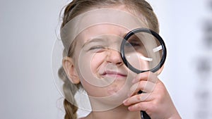 Curios female kid looking through magnifying glass, eyesight examination, health