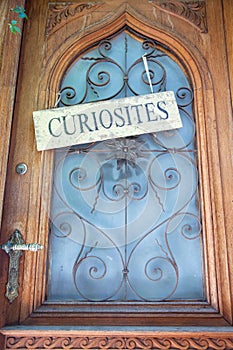 Curiosities sign hanging on wooden door with blue glass window and metal door handle