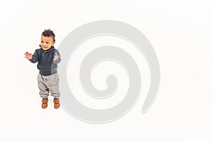 Curiosity concept. Young biracial toddler in warm clothes standing and clapping his hands over white background copy