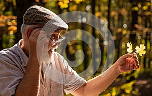 Curiosity to botany. Explore world around. Pensioner hiking in forest on sunny autumn day. Old man collect leaves