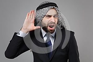Curious arabian muslim businessman in keffiyeh kafiya ring igal agal classic black suit isolated on gray background photo