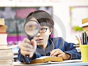 Curious asian pupil holding a magnifier in front of one eye