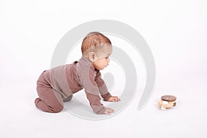 Curious baby boy crawling to wooden rattle toy