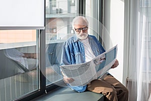 Curious bearded pensioner reading newspaper on windowsill