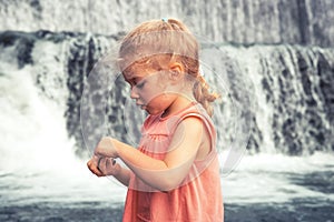 Curious beautiful child girl toddler portrait playing at waterfall during summer vacation concept happy childhood lifestyle