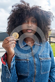 Curious Black Woman Holding Bitcoin Token in Urban Setting