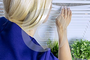 Curious blond woman peering through the white blinds