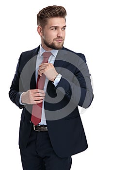 Curious businessman fixing his tie and looking over his shoulder