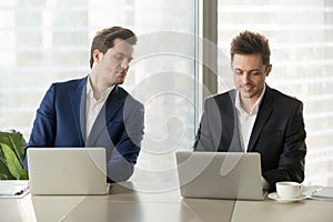 Curious businessman secretly looking at colleague laptop screen,