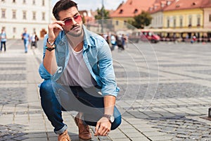 Curious casual man crouching in the city fixes red sunglasses