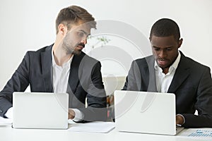 Curious Caucasian worker looking at African American colleague w photo
