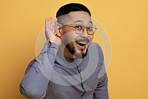 Curious Cheerful Asian Man Holding Hand Near Ear, Trying To Overhear Something