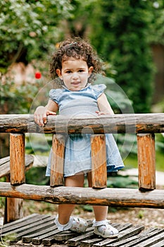 Curious child exploring nature, standing by a wooden fence in a lush green garden