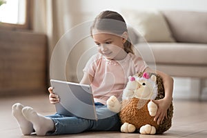 Curious child girl having fun using digital tablet embracing toy