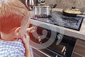 Curious child playing with the knobs on the oven. Danger for children at kitchen
