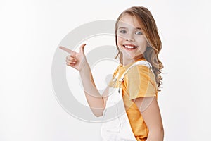 Curious clever pretty little girl found copy space, smiling amused and delighted, grinning playful, pointing left and