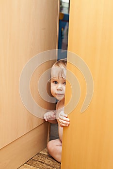 Curious cute baby boy looking through ajar door