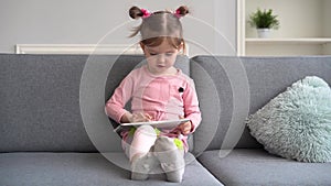 Curious cute baby girl using tablet. Lying on sofa alone