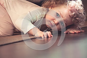 Curious cute child hiding under the bed in kids room and looking scared