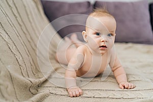 Curious cute little baby child lying on stomach on bed, interestingly looking at camera with open mouth. Carefree