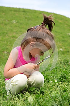 Curious Girl With Magnifying Glass Examining Flowers In The Grass At Spring Time