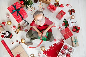 Curious girl wearing xmas costume reindeer antlers sitting on the floor, opening christmas present, top view.