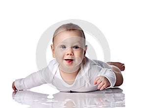Curious happy infant baby boy toddler in diaper and white bodysuit is lying on floor on his stomach crawling