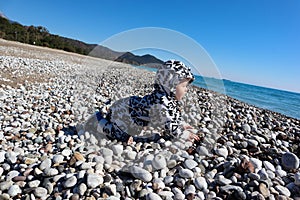 Curious happy little baby child crawling on the pebble beach under blue sky