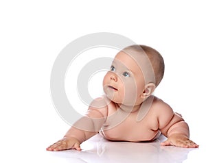 Curious infant child baby girl kid in diaper is lying on her tummy holding arm outstretched and looking at upper corner