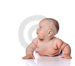 Curious infant child baby girl kid in diaper is lying on her tummy, stomach leaning, rising on hands and looking aside