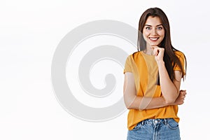 Curious and intrigued young woman listen interesting story, touch chin and smiling impressed, standing thoughtful