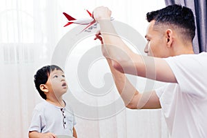 Curious kid looking at the plane toy and playing with father. Asian family playing toys together at home.