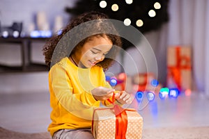 Curious little black girl opening gift box on Christmas Eve
