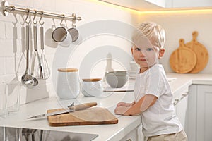 Curious little boy near kitchen counter with cutting board and sharp knife