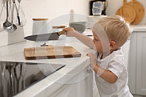 Curious little boy taking sharp knife from kitchen counter