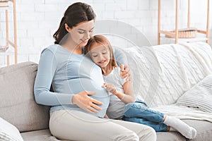 Curious little daughter touching her pregnant mother belly