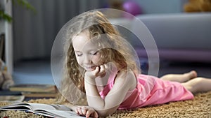 Curious little girl lying on floor, reading interesting childrens storybook