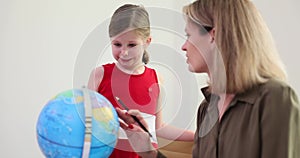 Curious little girl and mother learn about many places in world with globe at home