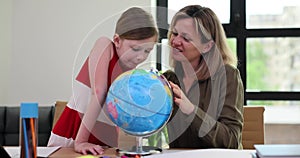 Curious little girl and positive woman look at globe at desk