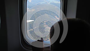 curious little passenger looks out of the plane window at beautiful view of mountains, child boy during an airplane