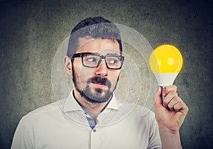 Curious man holding looking at bright light bulb