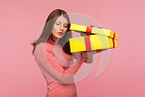 Curious nosy woman with brown hair in pink sweater unboxing big yellow present and secretly peeping inside