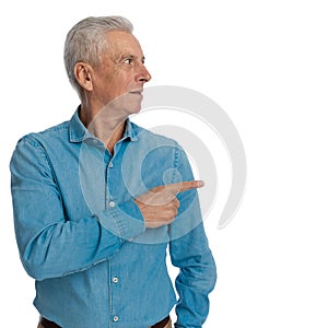 Curious old guy in jeans shirt looking and pointing finger to side