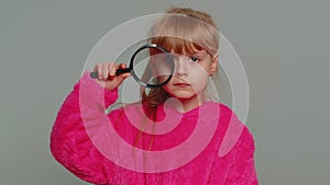 Curious preteen child girl kid holding magnifying glass near face funny eye searching analysing