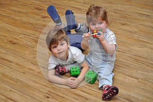 Curious siblings sitting and lying on wooden floor