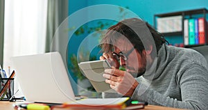 Curious, strange man working in office looks into a tablet, brings glasses closer to screen