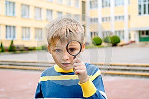 Curious surprised boy. One schoolboy with a magnifier near his eye in the school yard. young researcher, training and science.