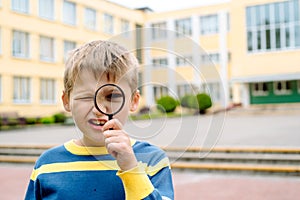 Curious surprised boy. One schoolboy with a magnifier near his eye in the school yard. young researcher, training and science.