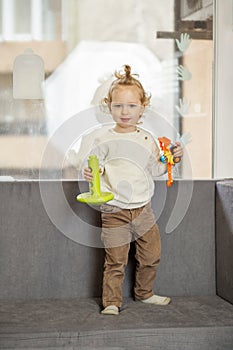 Curious Toddler Boy Holding Toys Standing on Couch