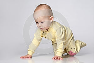 Curious Toddler infant kid crawling on a gray studio background, he dressed with yellow children's cotton overalls with